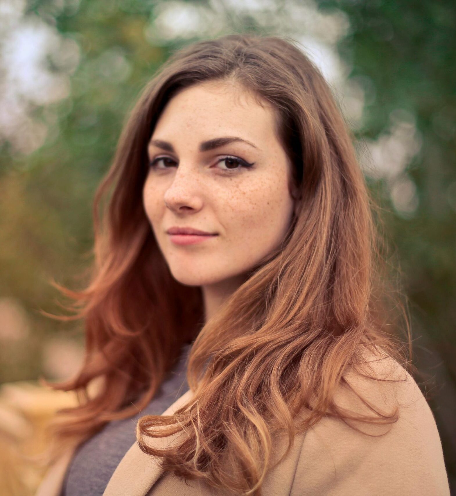 A young woman with long hair smiles confidently for an outdoor portrait session.